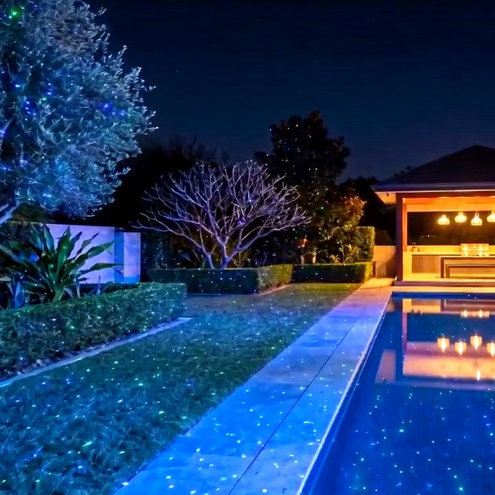 Real footage of green and blue laser stars across a poolside garden
