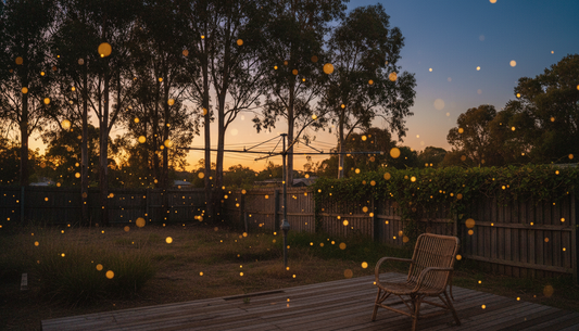 Australian backyard at dusk lit by yellow firefly garden lights — wooden deck and rattan chair