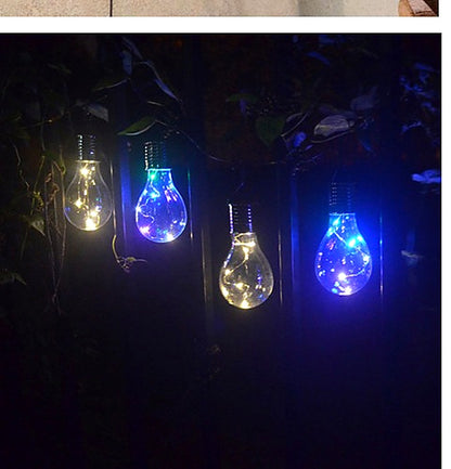 Solar hanging light bulbs glowing multicolour in a dark garden at night