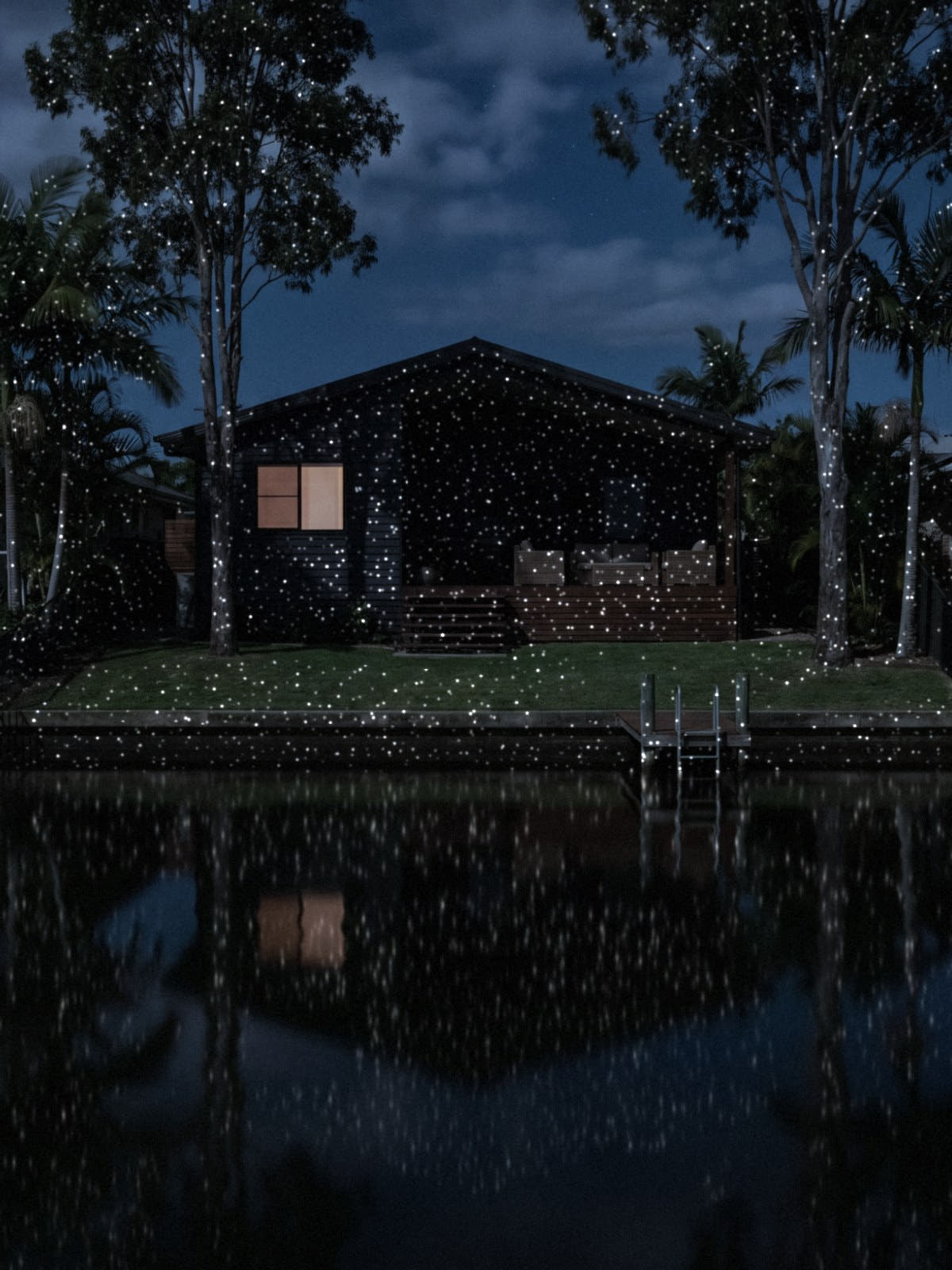 White Star laser points across a canal-front home, gum trees and lawn at night, reflected in the water