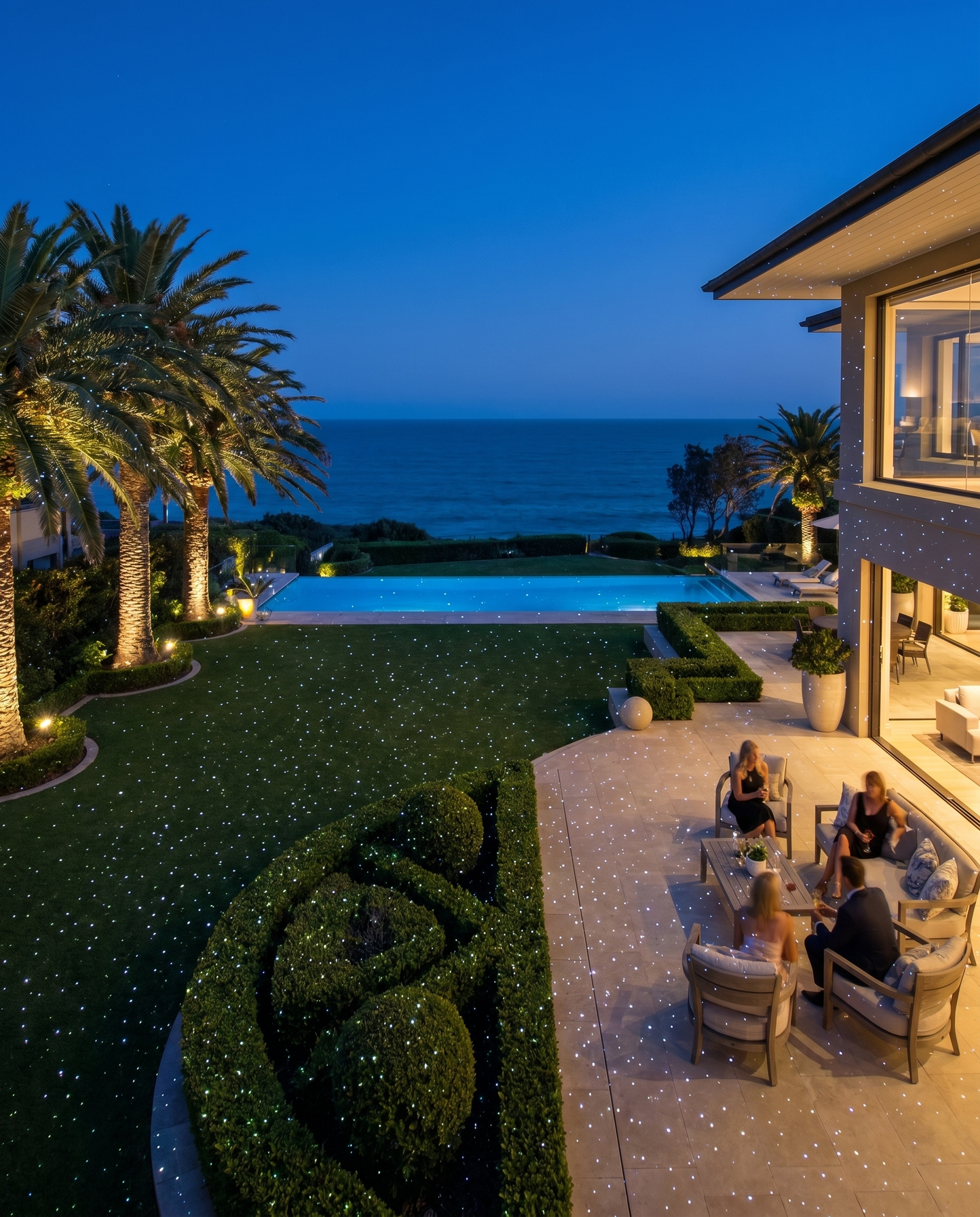 Coastal estate with infinity pool, lawn covered in white laser star points at night